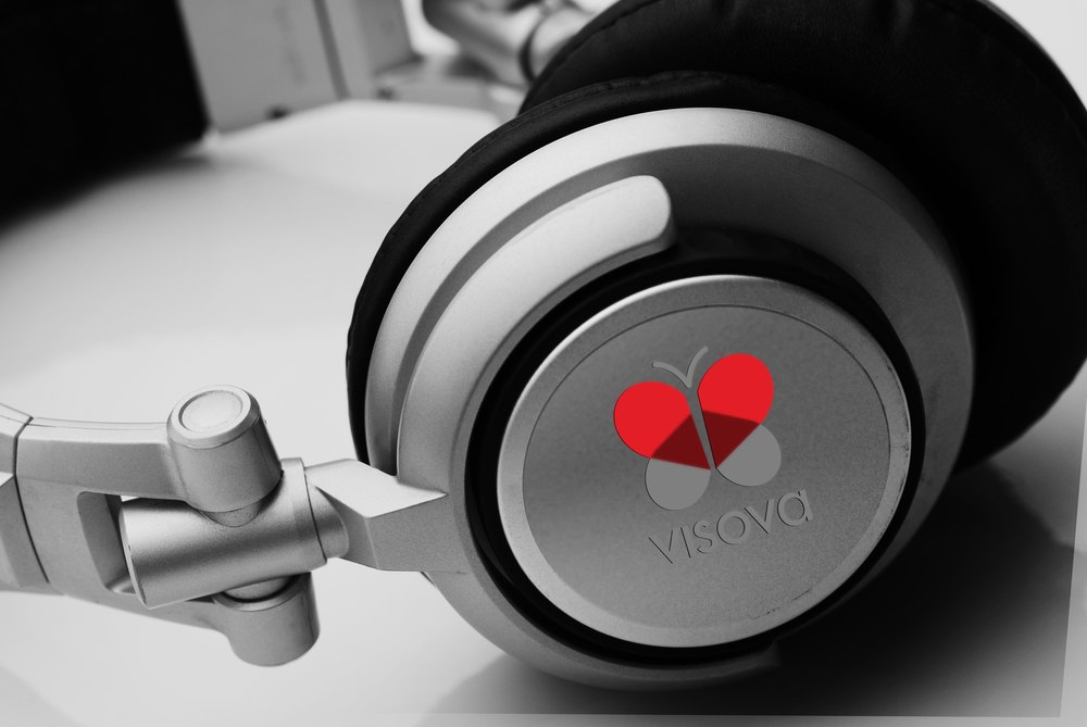 A pair of studio headphones photographed close in high-contrast black and white, ear cup toward the camera, with the red Visova butterfly mark sited in the center of the cup as the only color in the frame.