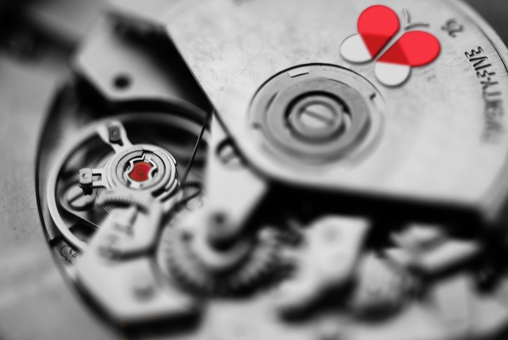 The exposed movement of a mechanical watch photographed in extreme close-up in high-contrast black and white, with the red Visova butterfly mark on the bridge plate and a single red jewel glowing in the gear train — the only two points of color in the frame.
